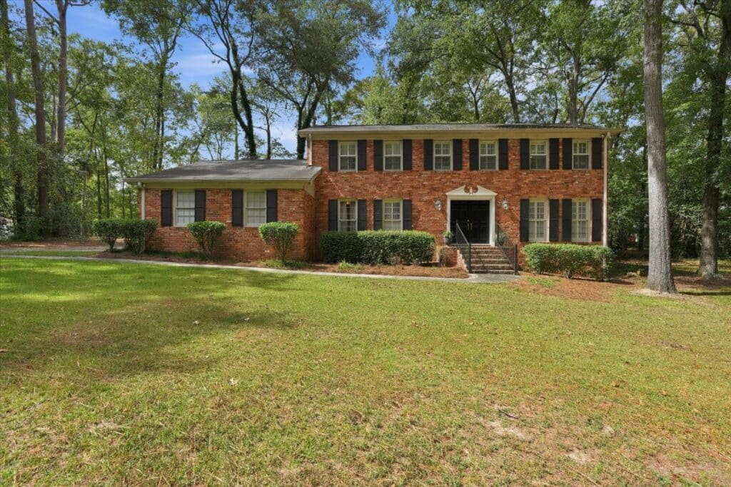 Front exterior of a two-story brick home with black shutters, mature trees, and a spacious front lawn at 176 Arlington Row in Castlegate, Macon, GA.